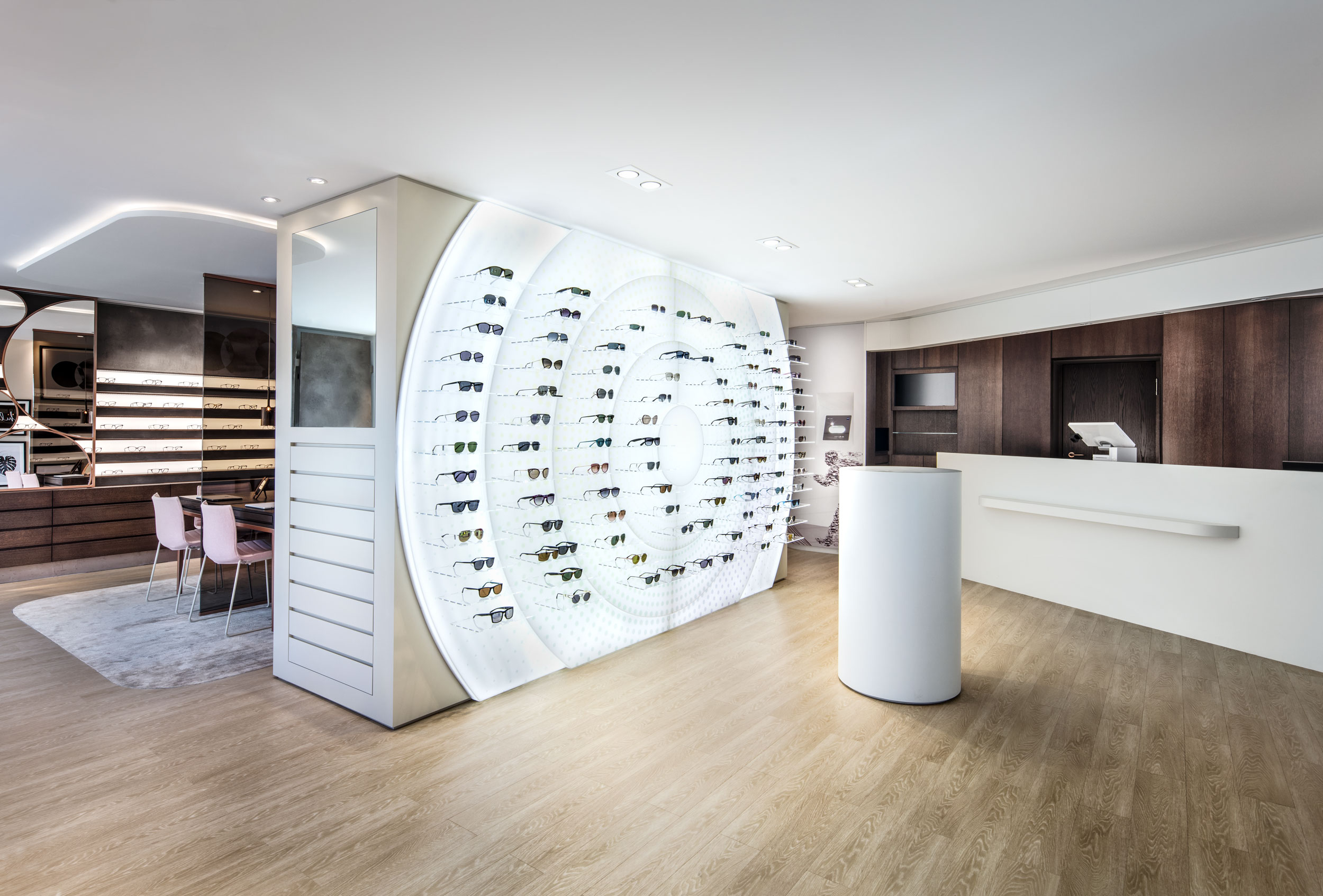 Weitwinkel-Aufnahme vom Eingangsbereichs des Showrooms mit beleuchteter Wand, an der eine große Auswahl an Sonnenbrillen präsentiert wird.