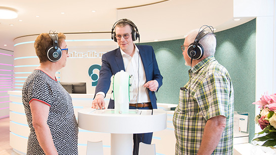 Sven Winkler steht mit zwei Kunden in der Filiale Wittlich um den Klangfinder