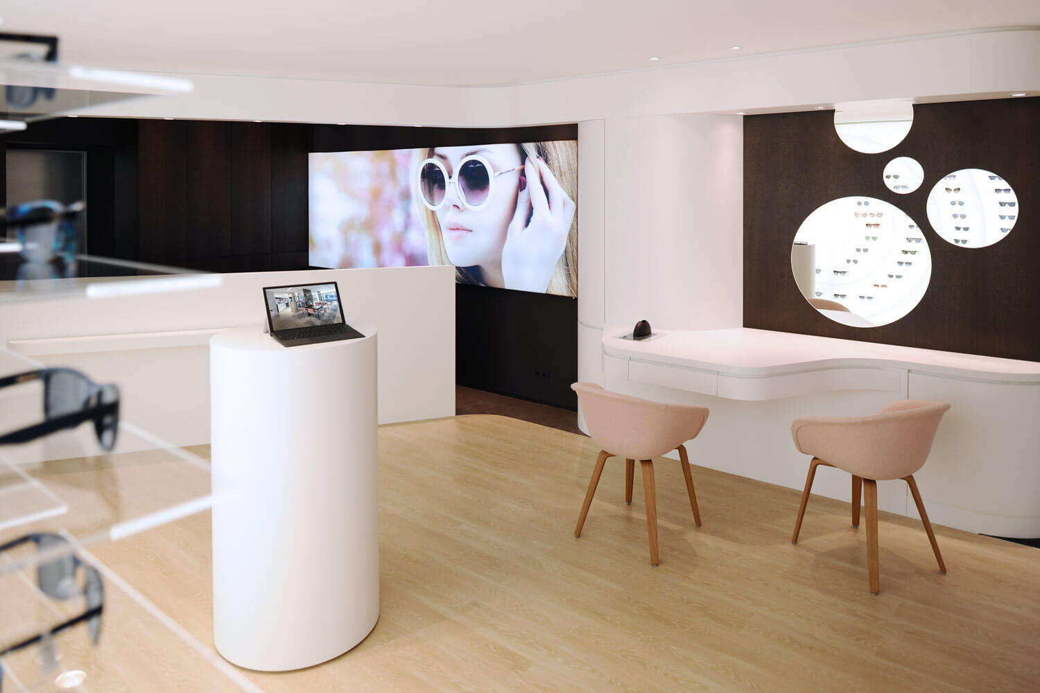 Weitwinkel-Aufnahme des Eingangsbereich des Showrooms mit Blick auf den Kassenbereich. Links ist eine Auswahl von Brillen zu sehen. Im Hintergrund ist ein großes Bild zu sehen, welches eine Frau mit Sonnenbrille zeigt.