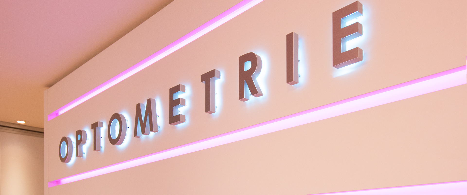 Nahaufnahme des Wortes OPTOMETRIE, welches als rückleuchtende Buchstaben an einer Wand montiert sind