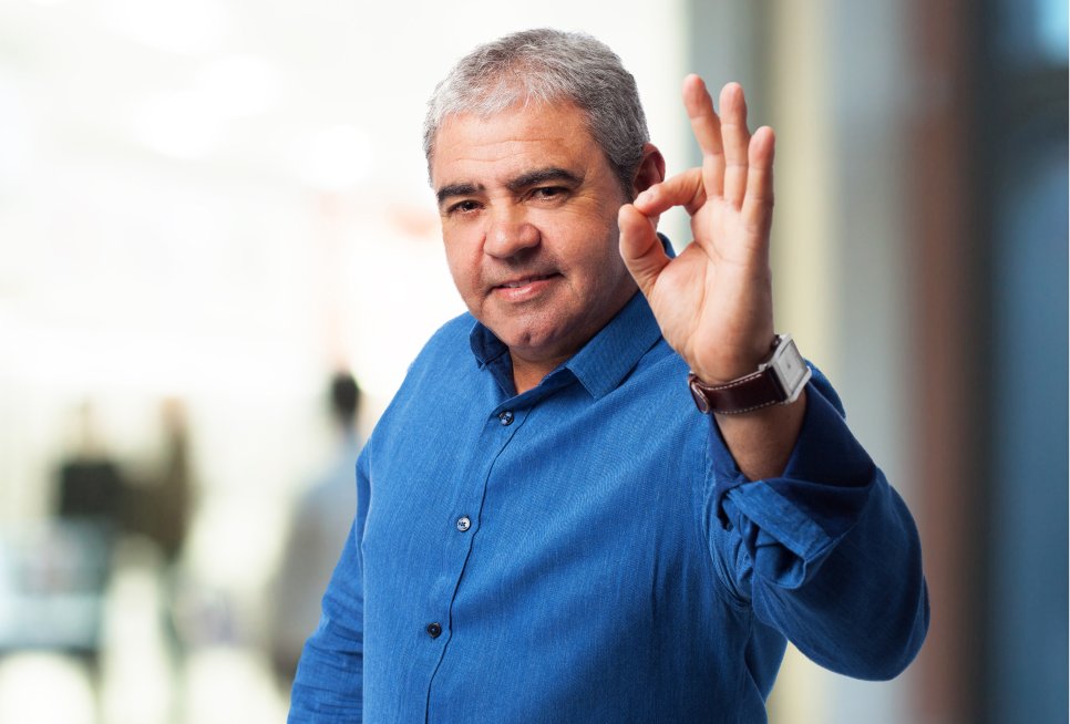 Ein älterer Mann, der das Handzeichen "OK" zum Betrachter zeigt.