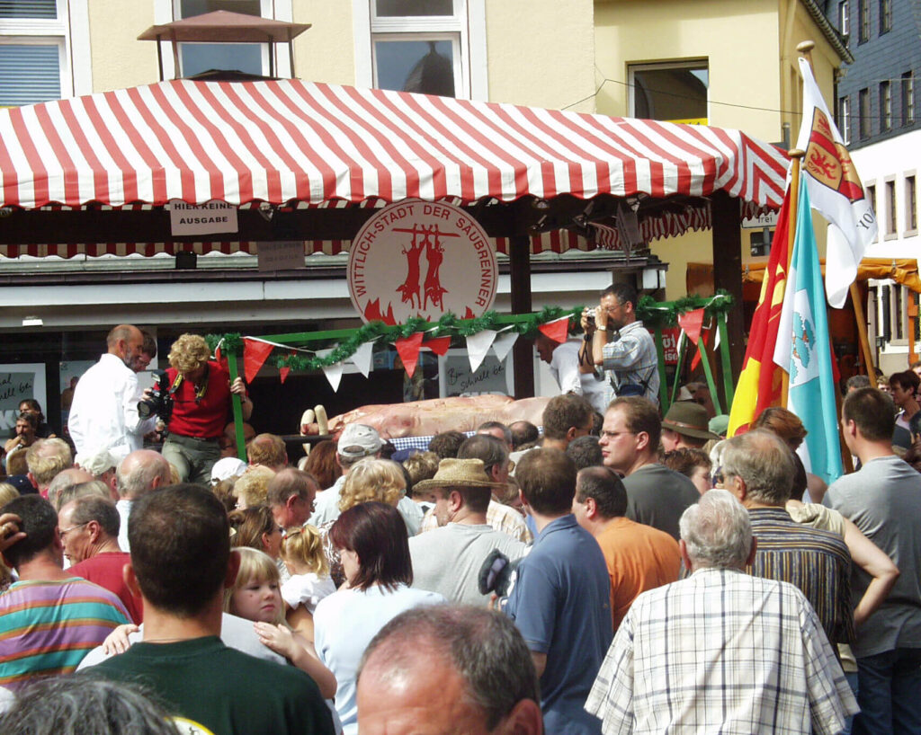 Menschenmenge vor dem Saubraten-Stand auf dem Marktplatz Wittlich. Im Hintergrund der Saubraten-Stand mit der Einfuhr der ersten Sau