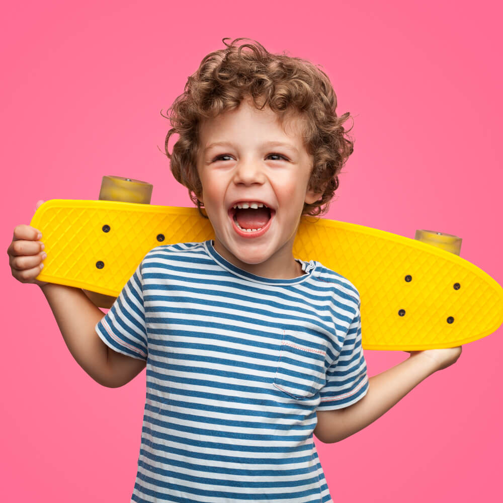 Ein lachender Junge hält hinter sich ein gelbes Skateboard