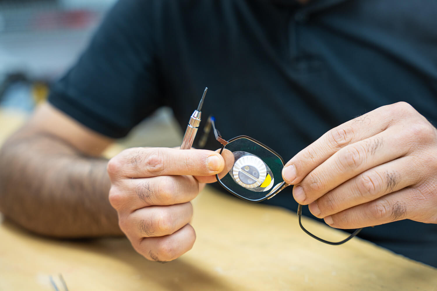 Brillengestell mit Halterung am Brillenglas, gehalten von einem Optiker. Dieser hält ein Präzision-Schraubendreher in der Hand