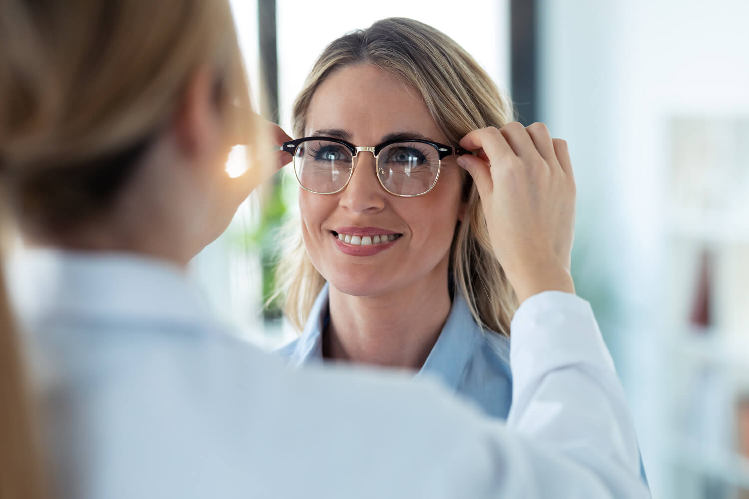 Junge Frau, die von einer Optikerin eine Brille aufgesetzt bekommt