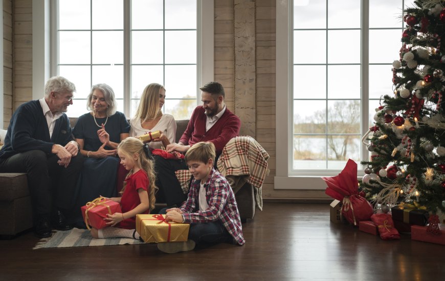 4 Erwachsene sitzen auf einem Sofa, im Vordergrund packen 2 Kinder Geschenke aus. Im rechten Bildbereich steht ein gescmückter Weihnachtsbaum