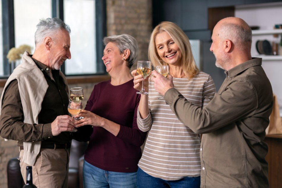 Eine Gruppe von vier Menschen in einer Wohnung, die mit Weißwein in Weingläsern anstoßen.