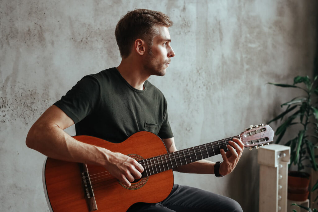 Junger Mann, der sitzend Gitarre spielt