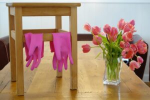 Tisch mit einer Vase mit Blumen und ein Hocker, an dem pinke Plastik-Handschuhe hängen